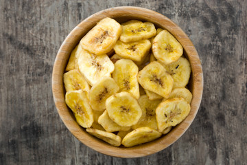 Banana chips in bowl on wooden table. Top view