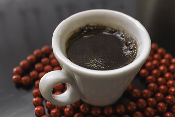 White cup of coffee on a dark surface surrounded by red beads