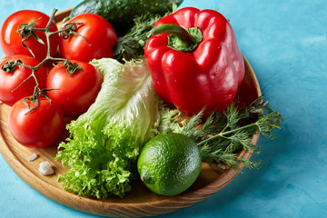 Refreshing close-up still life of assorted fresh vegetables and herbs on blue background, top view, selective focus.