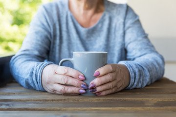 Hands of an elderly woman holding a cup of hot tea