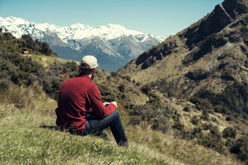 Naklejka na ściany i meble Hombre joven disfrutando de las vistas de un paisaje con montañas evadas en Nueva Zelanda