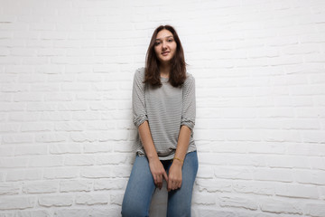 A young pretty smiling girl against a white loft-style brick wall. She looks at the viewer. Copy space.