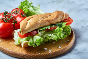 Fresh sandwich with lettuce, tomatoes and cheese served on wooden plate over white textured background, selective focus
