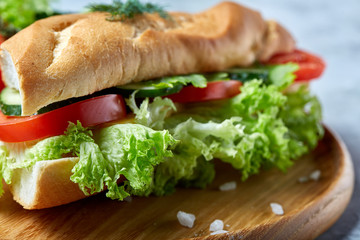 Fresh sandwich with lettuce, tomatoes and cheese served on wooden plate over white textured background, selective focus