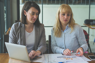 two attractive young woman working together with paperwork and using laptop to mentoring about some business planning at coffee shop.