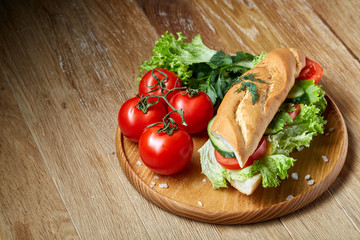 Fresh sandwich with lettuce, tomatoes, cheese on wooden plate, cup of coffee on rustic background, selective focus