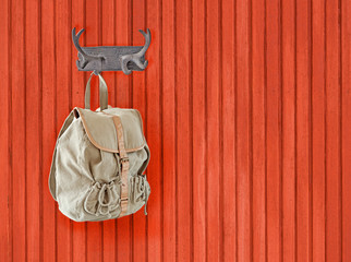 Backpack hanging on horn hanger on red painted wooden background.