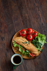 Fresh sandwich with lettuce, tomatoes, cheese on wooden plate, cup of coffee on rustic background, selective focus