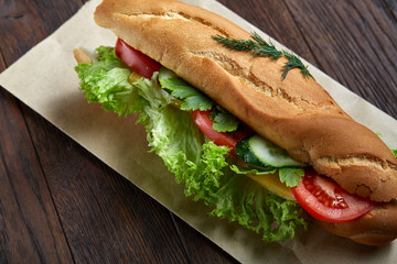 Fresh sandwich with lettuce, tomatoes, cheese on wooden plate, cup of coffee on rustic background, selective focus
