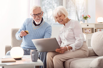 Fast payment. Cheerful senior man handing his credit card to his wife while they looking through an...