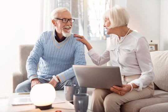 Good news. Joyful senior woman holding a laptop and laughing together with her husband while discussing the recent news, having read them online