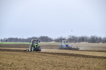 Obraz premium Lush and loosen the soil on the field before sowing. The tractor plows a field with a plow