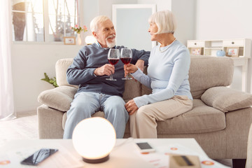 Romantic evening. Pleasant elderly couple sitting on the couch and drinking wine during the...