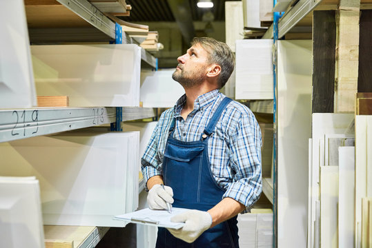Waist up portrait of mature worker holding clipboard making list of materials standing in storage room, copy space