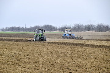 Obraz premium Lush and loosen the soil on the field before sowing. The tractor plows a field with a plow