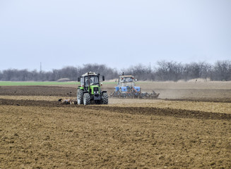 Obraz premium Lush and loosen the soil on the field before sowing. The tractor plows a field with a plow