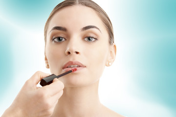 Young woman applying lipstick against blue isolated background