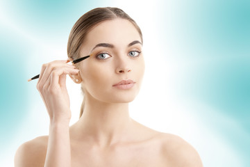 Fototapeta premium Studio shot of a beautiful young woman applying makeup to her eyebrow while standing at isolated background.
