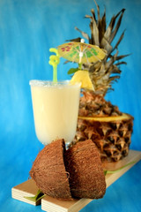Milk fruit cocktail in an Irish mug decorated with a piece of pineapple, an umbrella and a straw on blue background