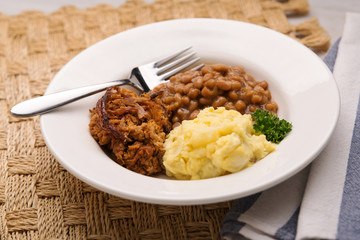 Pulled pork, beans and potato salad in a white bowl