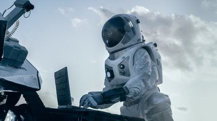 Astronaut in the Space Suit Works on Laptop, Adjusting Rover on a New Alien Planet. Day Light High-Tech Space Exploration Concept. Manned Mission Searching and Discovering New Habitable Planets.