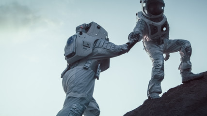 Two Astronauts Climbing Mountain Hill Helping Each Other, Reaching the Top. Overcoming...