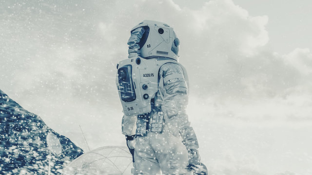 Shot of the Astronaut Looking Through the Snow Storm on Frozen Alien Planet. In the Background His Base/ Research Station. Technological Advance Brings Space Exploration, Colonization.