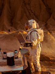 Astronaut in the Space Suit Works on Laptop, Adjusting Rover For Mars further Mars Exploration.Space Exploration Concept.First Manned Mission on Red Planet. © Gorodenkoff