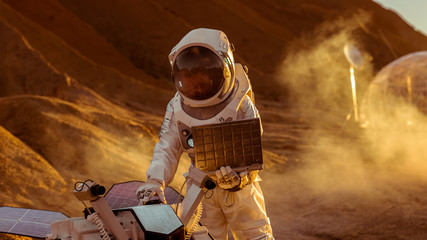 Astronaut in the Space Suit Works on Laptop, Adjusting Rover For Mars further Mars Exploration.Space Exploration Concept.First Manned Mission on Red Planet.