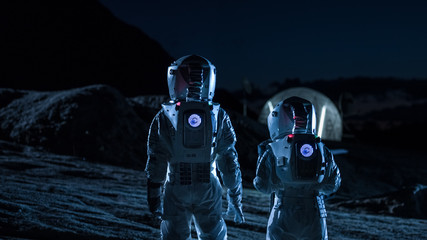 Two Astronauts in Space Suits Walk on the Alien Planet Looking at the Sky. In the Background Base with Geodesic Dome. Other Worlds Colonization and Space Travel Concept. © Gorodenkoff