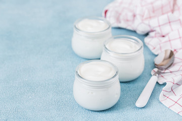 Obraz na płótnie Canvas Homemade coconut yogurt in glass jars on light blue background. Selective focus, copy space.