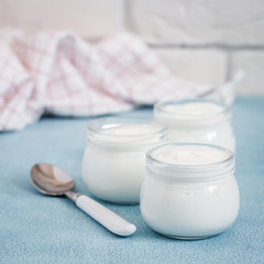 Homemade sour cream in glass jars on light blue background. Selective focus, copy space.