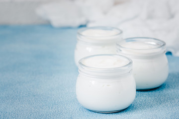 Homemade yogurt in glass jars on light blue background. Selective focus, copy space.