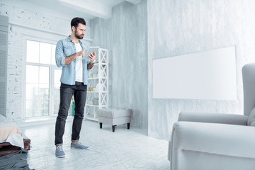 Creating plan. Serious male person holding gadget in left hand and bowing head while reading news