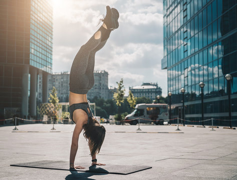 Young athletic woman doing handstand on city street among modern skyscrapers. Workout. Exercise for balance, yoga.