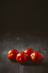 Four tomatoes on a black wooden background.