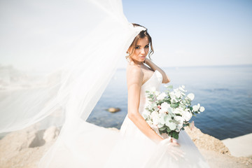 Beautiful young bride with bridal bouquet posing on the background sea