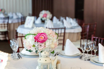 Glasses, flowers, fork, knife, napkin folded in a pyramid, served for dinner in restaurant with cozy interior. Wedding decorations and items for food, arranged by the catering service on a large table