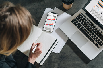 View from above. Girl is making a notes in notebook, planning. Student learning, doing homework. Near on table laptop.