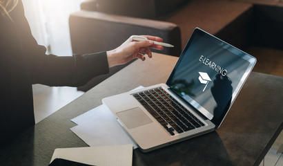 Woman standing near table,pointing pencil on laptop with inscription on screen e-learning, image of square academic cap