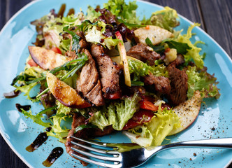 Veal salad with lettuce, apple, pear and tomato on blue plate on dark wooden background, copy space. Restaurant food, close up. Meat salad