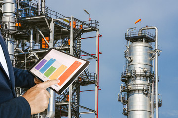 businessman fingers touching chart tablet against oil refinery in petrochemical Aerial view oil refinery night during twilight,Industrial zone,Energy power station 