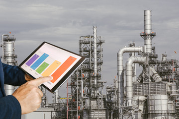 businessman fingers touching chart tablet against oil refinery in petrochemical Aerial view oil...