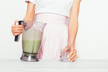 Slender young woman in a pink skirt pours a green smoothie