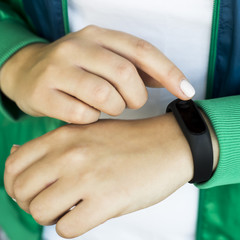 A woman clicks on her smart fitness bracelet. In a sports bright green jacket for sports. Healthy lifestyle and fitness concept