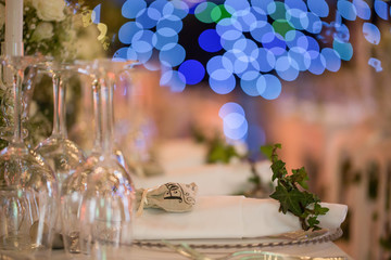 Wedding table with bokeh blue lights. Closeup of glasses and plate with blurry background. Love concept.