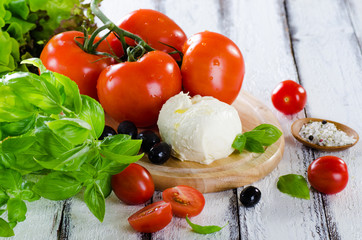 Fresh tomatoes, mozarella and basil ingredients fir salad on white wooden background