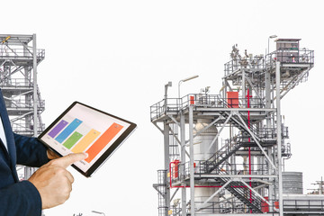 businessman fingers touching chart tablet against oil refinery in petrochemical Aerial view oil refinery night during twilight,Industrial zone,Energy power station 