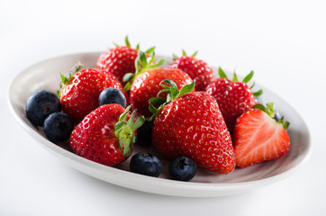 Fresh ripe strawberries and blueberries in a bowl on white background