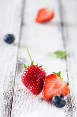 Fresh ripe strawberries and blueberries on plate on white wooden rustic background